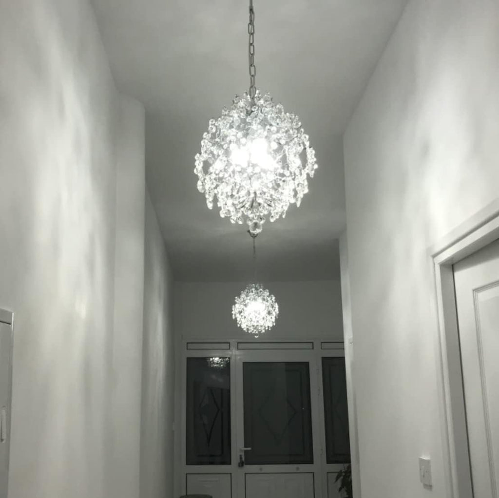Two Maison Ornate Crystal Ball Chandeliers with triple drop shades, emitting bright white light.