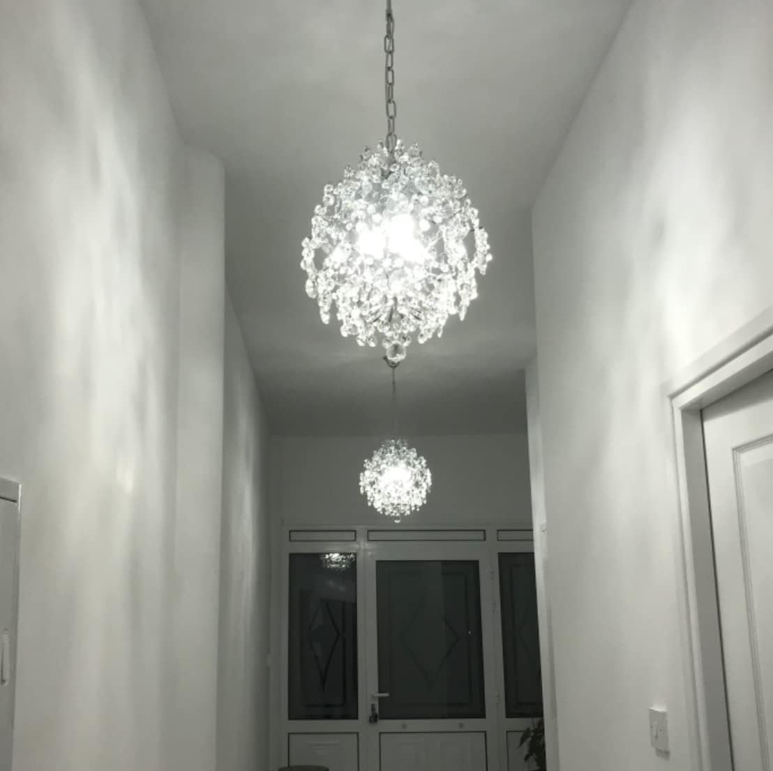 Two Maison Ornate Crystal Ball Chandeliers with triple drop shades, emitting bright white light.
