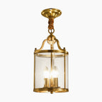 Modern gold chandelier with cylindrical glass shade, three candle bulbs, brass canopy, and twisted brown rope.