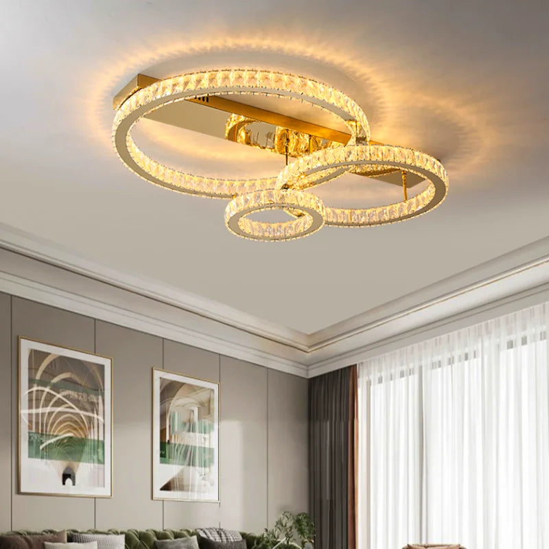 Three circular stainless steel chandelier rings edged in crystals, emitting a warm, modern glow.