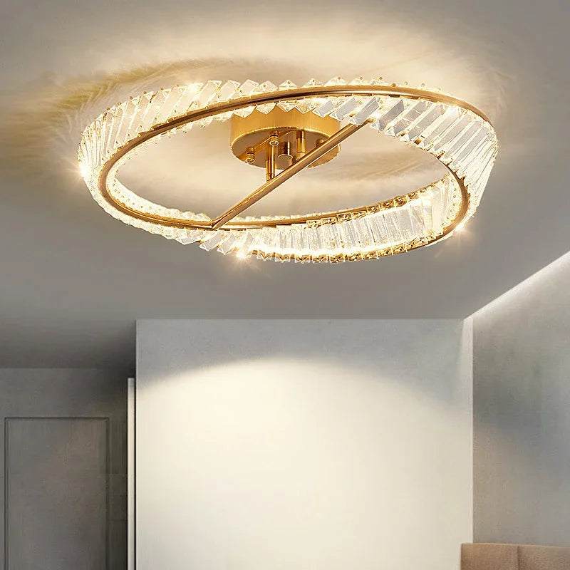 Gold-base chandelier with overlapping crystal rings emits warm light; elegant, modern, dimmable LED design.