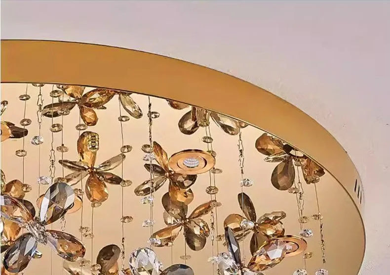 Gold circular chandelier with hanging crystal and gold floral accents, reflecting elegant, luxurious light.
