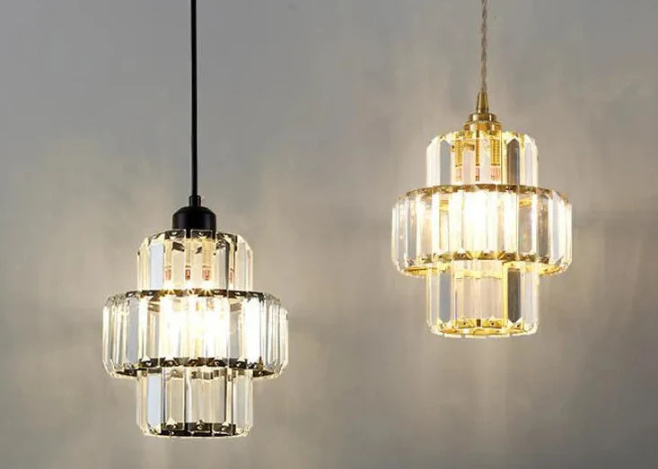 Maison Ornate K9 Crystal Art Deco pendant lights: one black metal, one gold, glowing warmly.