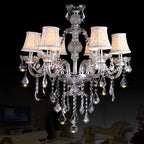 Eight-arm crystal chandelier with white patterned shades and tassels, European-inspired, elegant lighting fixture.