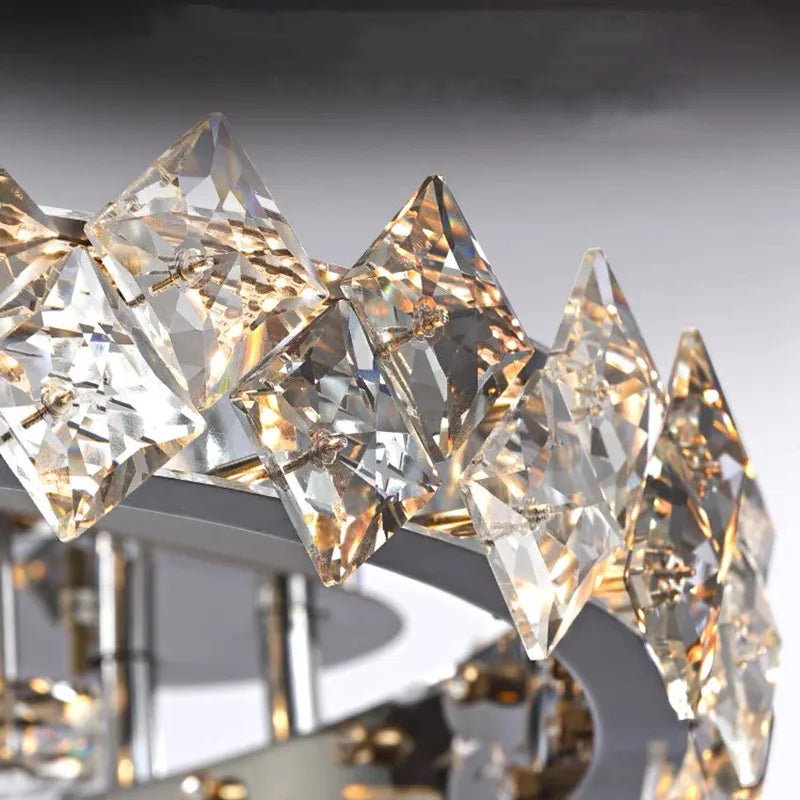 Close-up of circular stainless steel chandelier with diamond-shaped crystal prisms and warm LED lighting.