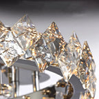 Close-up of circular stainless steel chandelier with diamond-shaped crystal prisms and warm LED lighting.