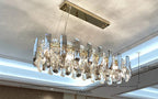 Rectangular gold-accented chandelier with vertical crystal prisms, LED-lit, 23x80 cm, warm elegant glow.