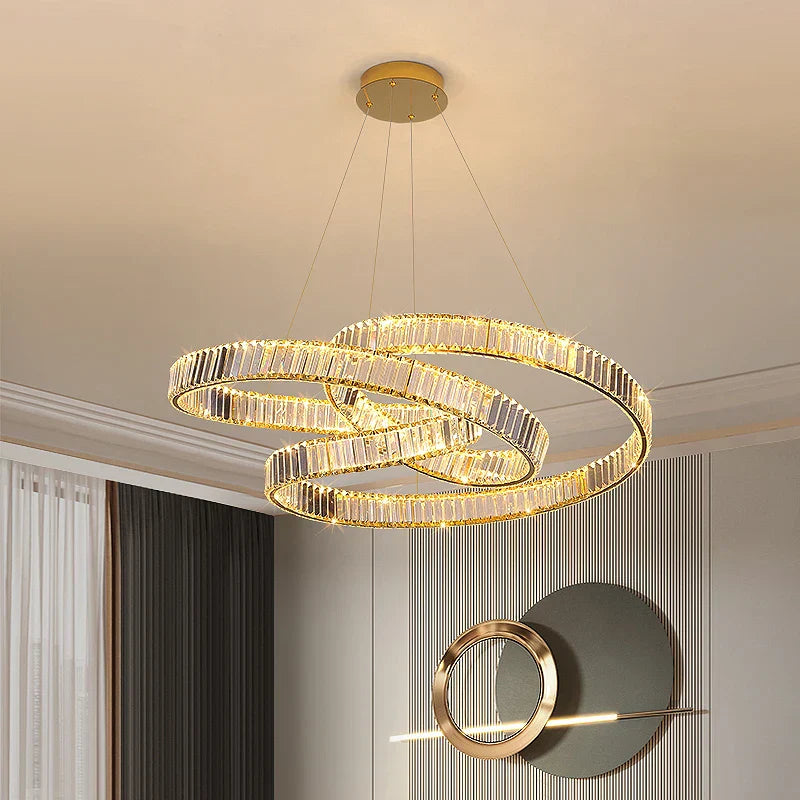 Three intertwined gold crystal rings form a minimalist LED chandelier, suspended by slender wires.