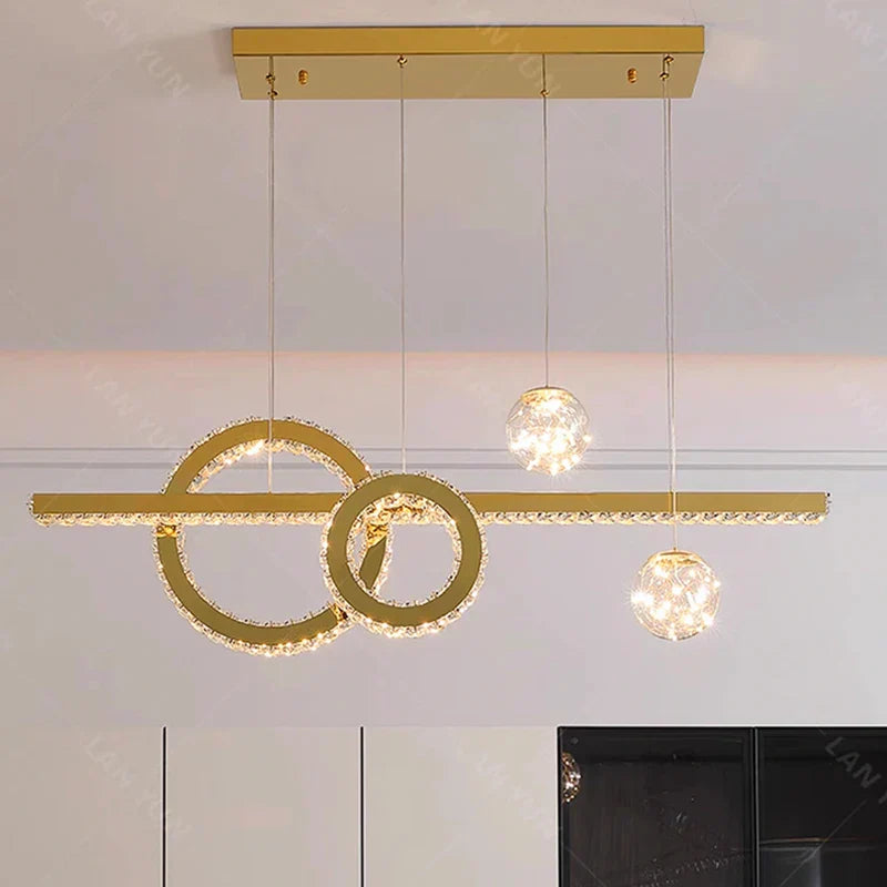 Contemporary chandelier with interlocking gold rings, crystal bar, and three crystal pendants. Elegant lighting fixture.