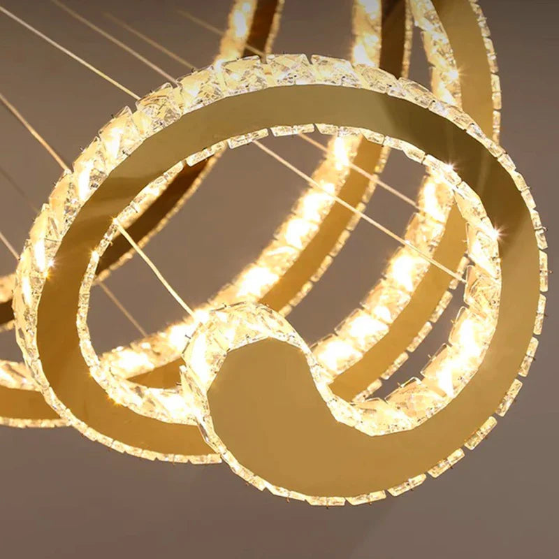 Elegant gold ring chandelier with crystal edges, suspended by wires and warm LED lighting.