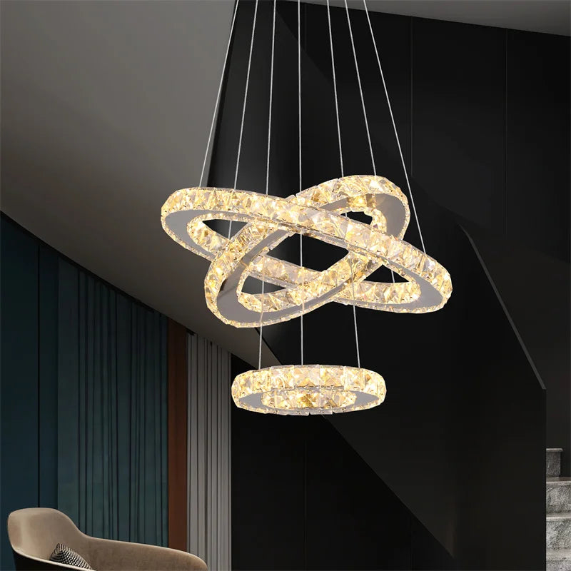 Three illuminated crystal-encrusted rings suspended at varied angles create an Art Deco-inspired chandelier.