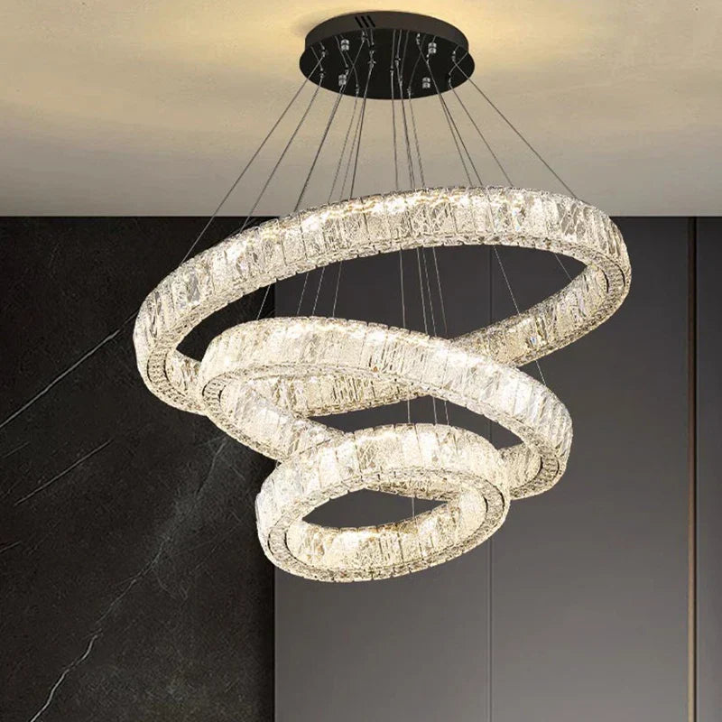 Three illuminated crystal rings intertwine in a pendant chandelier, suspended by thin wires.