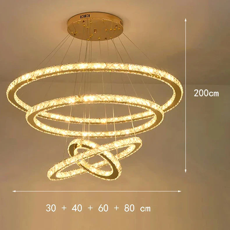 Gold-base chandelier with four crystal rings, dimmable LED, adjustable height up to 200 cm.
