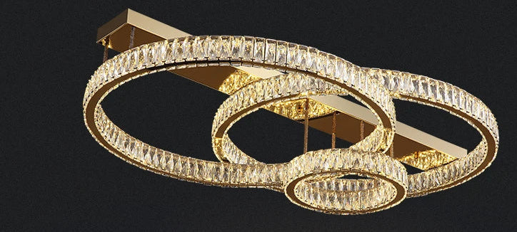 Three gold intersecting crystal-accented rings suspended from a gold rectangular ceiling light base.