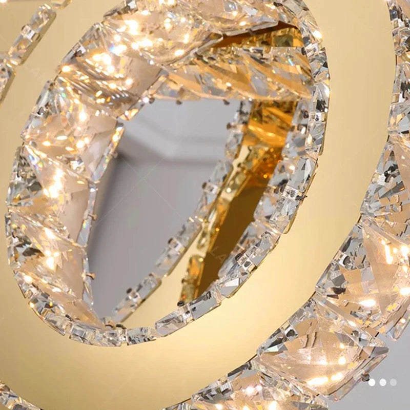 Intertwined gold and crystal rings with embedded LEDs create a sparkling, elegant chandelier.