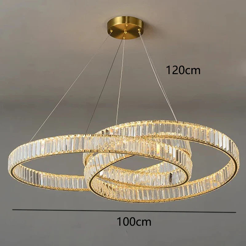 Three gold-edged crystal rings form a modern chandelier, emitting warm light; elegant and luxurious.