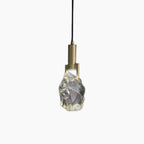 Modern copper chandelier with crystal-like glass shade, suspended by black cord; minimalist, elegant design.