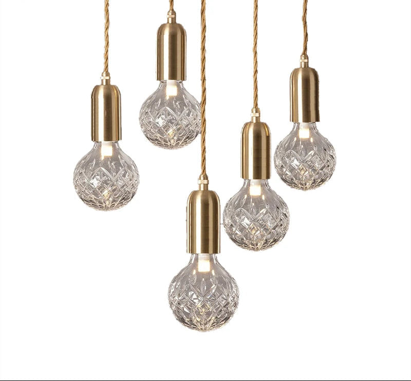 Five crystal-patterned bulbs with gold sockets hang from twisted cords, forming a modern chandelier.