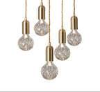 Five crystal-patterned bulbs with gold sockets hang from twisted cords, forming a modern chandelier.