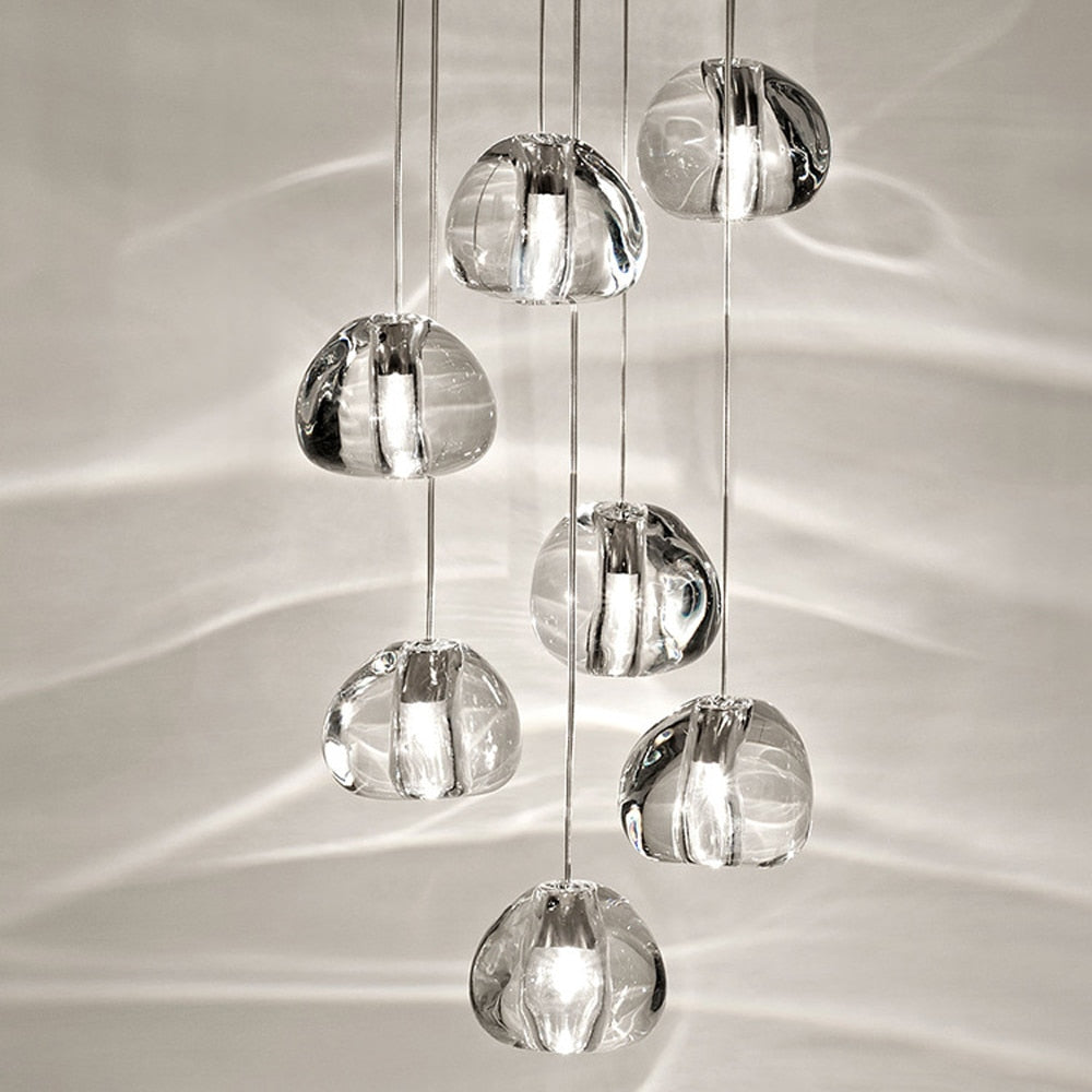 Eight rounded glass crystal pendant lights hang at different heights on slender cords, softly glowing.