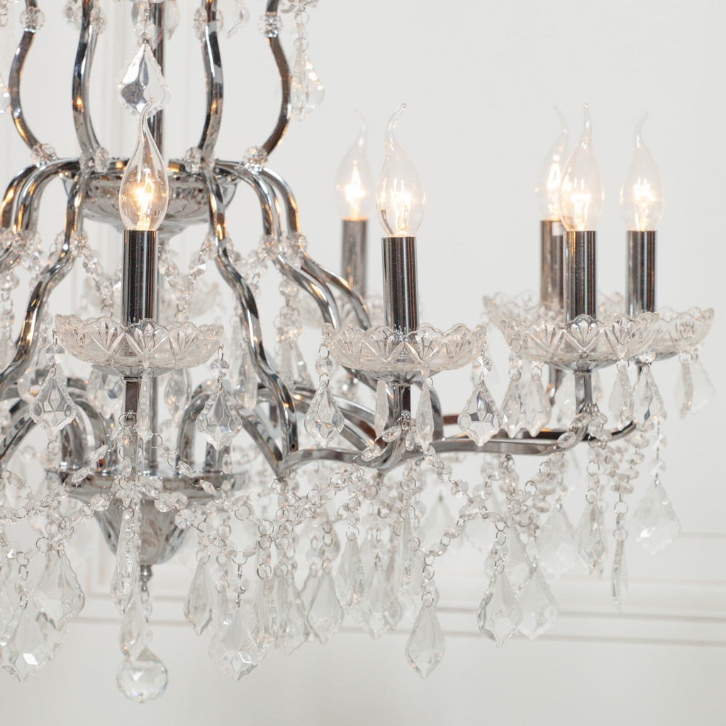 Close-up of Maison Ornate 12-arm chrome chandelier with lit candle bulbs and hanging clear crystals.