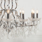 Close-up of Maison Ornate 12-arm chrome chandelier with lit candle bulbs and hanging clear crystals.