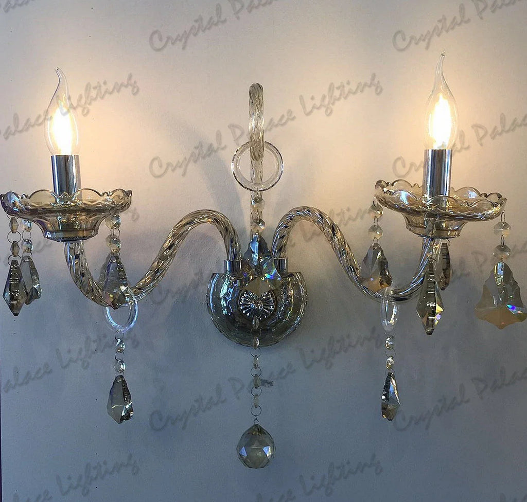 Two-arm chandelier sconce with candle-style bulbs, K9 crystal pendants, and shiny champagne finish.