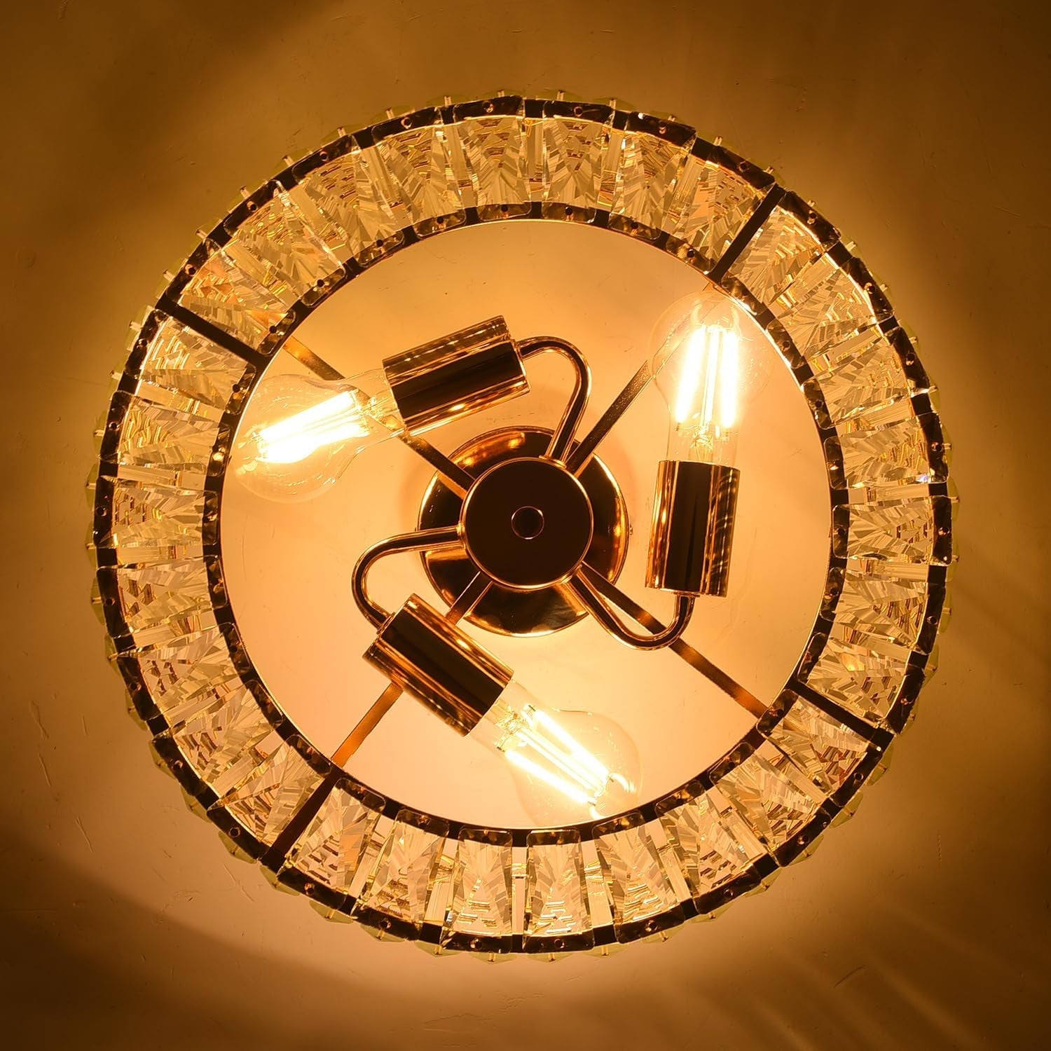 Close-up of gold 3-light crystal chandelier with exposed bulbs and metal accents, glowing warmly.